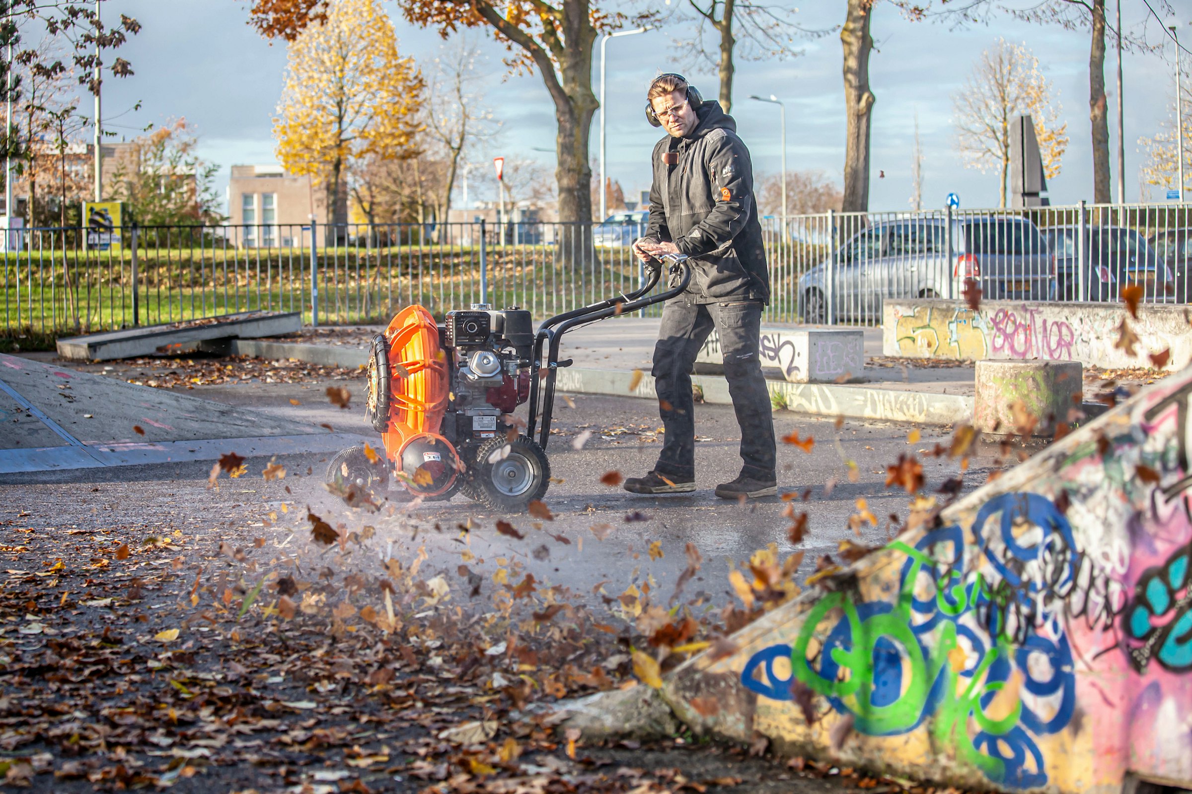 Man using force blower pictured from the side blowing leaves and dust on pavement